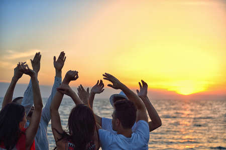 group of happy young people dancing at the beach on beautiful summer sunsetの写真素材