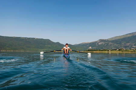 A Young single scull rowing competitor paddles on the tranquil lake