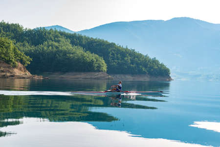 A Young single scull rowing competitor paddles on the tranquil lakeの写真素材