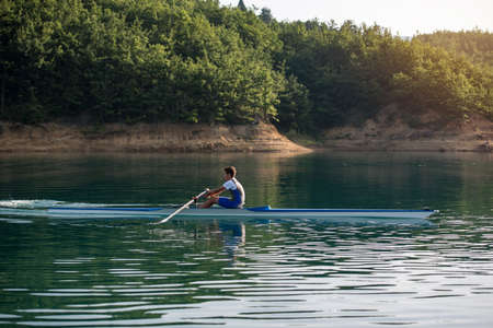 A Young single scull rowing competitor paddles on the tranquil lakeの写真素材