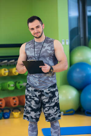 Portrait of a muscular trainer writing on clipboardの写真素材