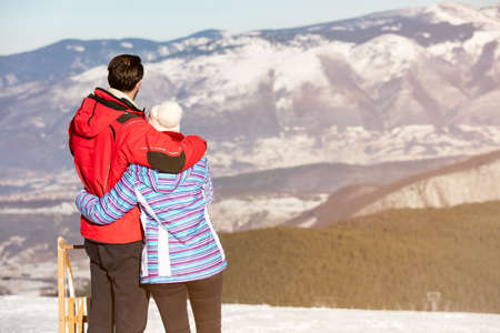 Rear view of a loving couple in fur hood jackets looking at snowed mountain rangeの写真素材