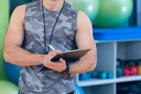 Portrait of a muscular trainer writing on clipboardの写真素材