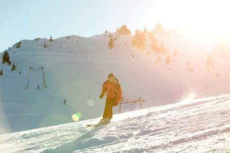Skier skiing downhill in high mountains against sunsetの写真素材