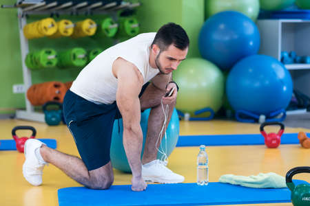 Male athlete kneeling down by dumbbells toweling sweat of his brow.の写真素材