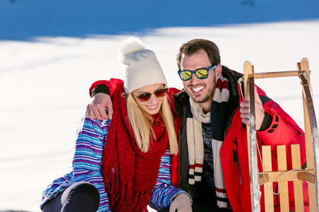 Young playful couple having fun sledging down snow covered hill