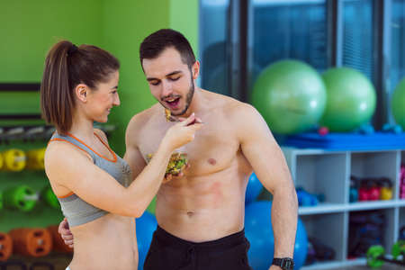 Happy couple in gym feeding each other with fresh saladの写真素材