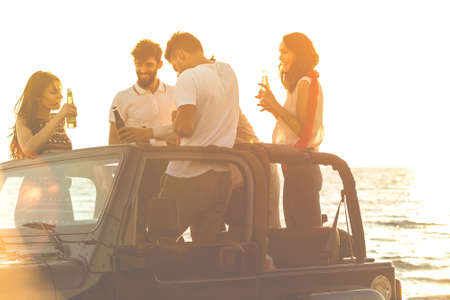 Five young people having fun in convertible car at the beach at sunset.の写真素材