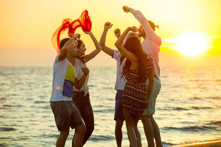 group of happy young people dancing at the beach on beautiful summer sunsetの写真素材