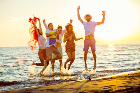 group of happy young people dancing at the beach on beautiful summer sunsetの写真素材