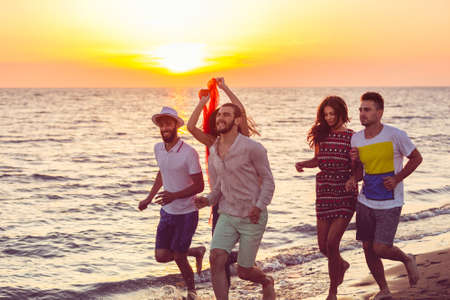 Group of happy young people is running on background of sunset beach and seaの写真素材