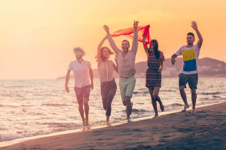 Group of happy young people is running on background of sunset beach and seaの写真素材