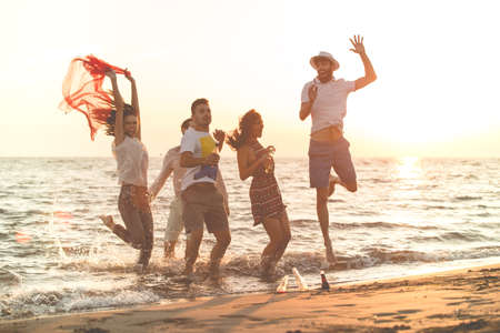 group of happy young people dancing at the beach on beautiful summer sunset