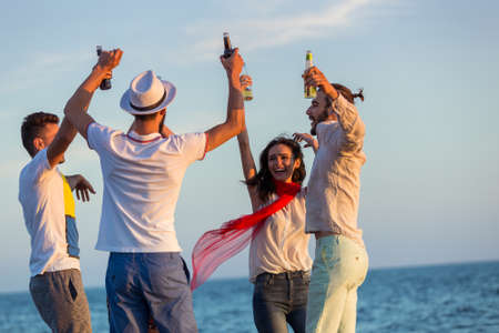 group of happy young people dancing at the beach on beautiful summer sunsetの写真素材