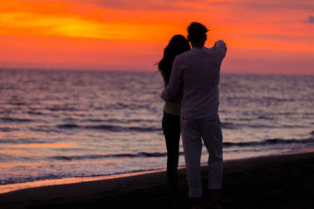sunset silhouette of young couple in love hugging at beach