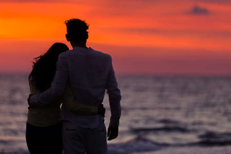 sunset silhouette of young couple in love hugging at beachの写真素材