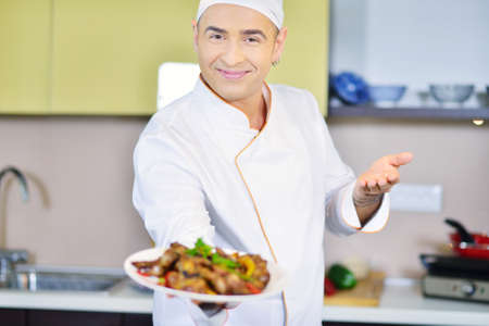 Cook holding plate with food in welcoming gesture
