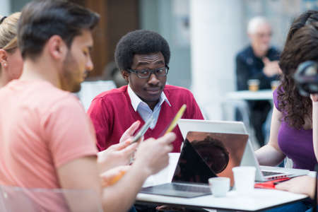 A group of teenagers sitting at the table in cafe, using laptop and drinking orange juice.