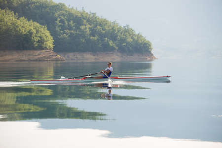 A Young single scull rowing competitor paddles on the tranquil lake
