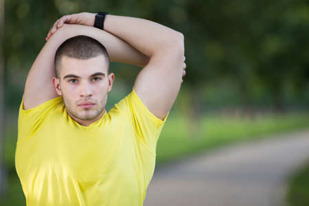Fitness man stretching arm shoulder before outdoor workout. Sporty male athlete in an urban park warming up.の写真素材