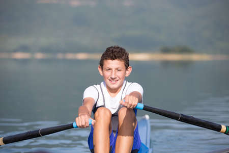 A Young single scull rowing competitor paddles on the tranquil lakeの写真素材