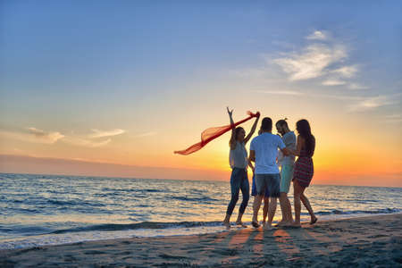 group of happy young people dancing at the beach on beautiful summer sunset.の写真素材