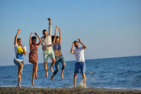 Group of friends having fun walking down the beach at sunsetの写真素材