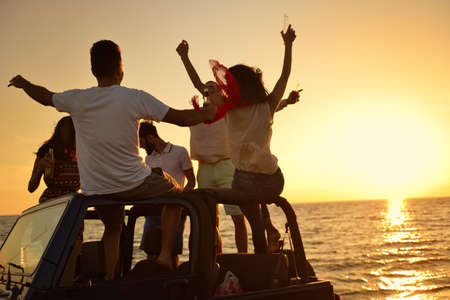 Five young people having fun in convertible car at the beach at sunset.の写真素材