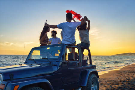 Five young people having fun in convertible car at the beach at sunset.の写真素材