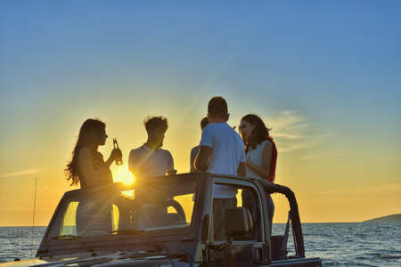 Five young people having fun in convertible car at the beach at sunset.の写真素材
