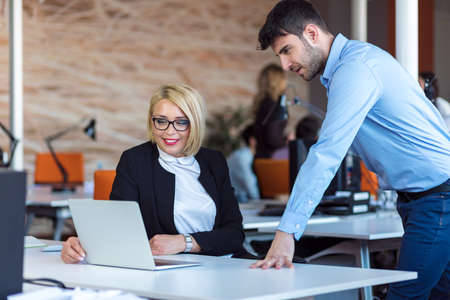 Colleagues chatting, sitting together at office table, smiling