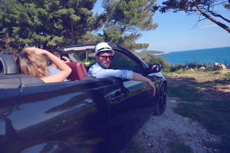 leisure, road trip, travel and people concept - happy friends driving in cabriolet car along country roadの写真素材