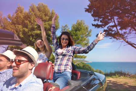leisure, road trip, travel and people concept - happy friends driving in cabriolet car along country roadの写真素材