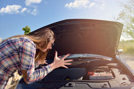 Women spection She opened the hood Broken car on the side See engines that are damaged or not.