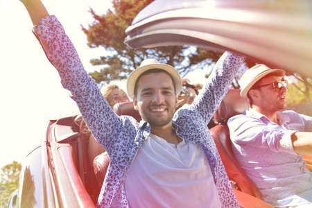 leisure, road trip, travel and people concept - happy friends driving in cabriolet car along country roadの写真素材