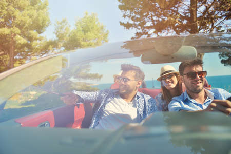 leisure, road trip, travel and people concept - happy friends driving in cabriolet car along country roadの写真素材