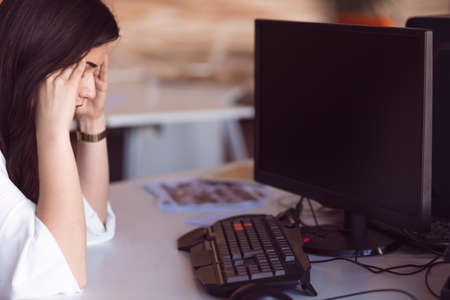 Young tired business woman with headache sitting in workplace