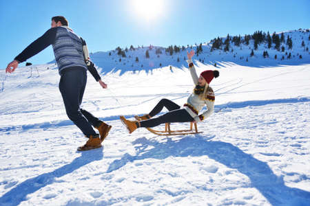 Young Couple Sledding And Enjoying On Sunny Winter Day