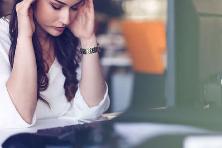 Young tired business woman with headache sitting in workplaceの写真素材