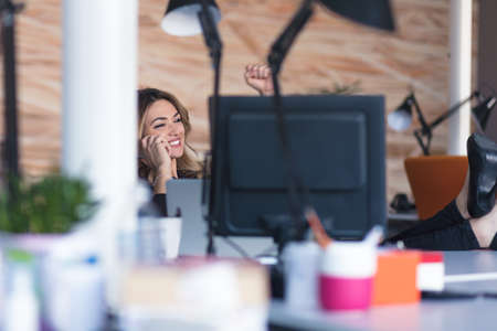 Beautiful young woman working on computer and talking on phoneの写真素材