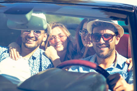 Group of cheerful young friends driving car and smiling in summerの写真素材