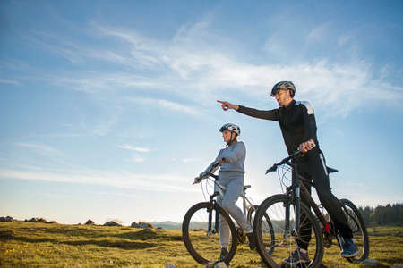 Biker couple with mountain bike pointing in distance at countrysideの写真素材