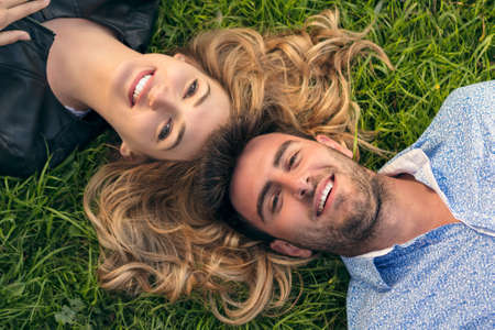 Happy Smiling Couple Relaxing on Green Grass.Park.Young Couple Lying on Grass Outdoor. Elegantly...