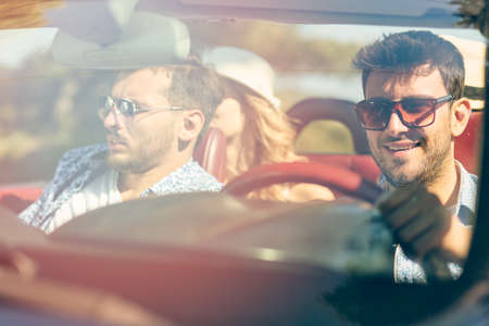 Group of cheerful young friends driving car and smiling in summerの写真素材