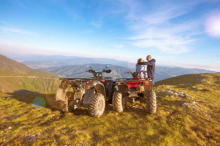 Rear view of young pair near atv. Man is showing something in distance to her girlfriend.