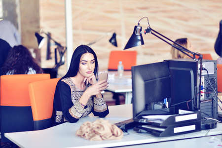Portrait of young bored attractive woman at office desk, with laptop, looking for some good musicの写真素材