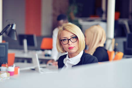 Beautiful young woman holding hands on chin and smiling while sitting at her working placeの写真素材