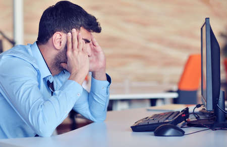 Businessman feeling headache while doing distance work in coffee shop tired with failure of plansの写真素材