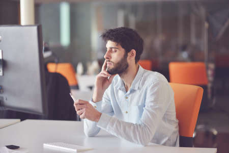 young business man working on desktop computer at his desk in modern bright startup office interiorの写真素材