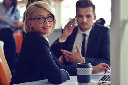 Beautiful young business partners are using a laptop, discussing documents and smiling while working in office.の写真素材